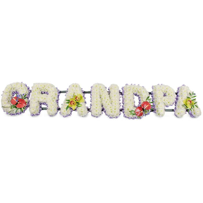 Spanning the width of the image, this carefully constructed sympathy tribute spells GRANDPA in strong block capitals, designed to rest on a stand at the front of a funeral or memorial in Friern Barnet. Every letter is built on a sturdy frame, which is then completely covered with neat, tightly packed white chrysanthemums. Their petite, multi-petalled heads overlap to form a seamless carpet of blooms, giving the letters a plush, padded appearance that feels calm and gentle, almost like a soft, floral cushion. The dominance of white suggests purity, peace, and a quiet farewell. At the base of each letter, you can glimpse a fine edging of pale lavender ribbon, the cool purple tone providing a subtle contrast that outlines the shapes without overwhelming them. Hidden behind and underneath, green support bars link the letters, ensuring that the whole word stays perfectly aligned for delivery to local churches and venues from Friern Barnet to nearby Bounds Green. Accents of colour add depth and individuality: the 'G' and 'D' are highlighted with rich red anthuriums, their shiny, heart-shaped blooms and upright yellow spadices framed by polished green foliage and possibly tiny touches of complementary filler, creating focal points of warmth and remembrance. The first and last 'A' are adorned with clusters of yellow-green orchids, their graceful, exotic flowers and buds tucked into lush greenery, introducing a note of elegance and enduring affection. Altogether, the tribute feels both strong and tender, a bespoke floral word that allows families in Friern Barnet to honour a beloved grandfather with a clear, visible expression of love, respect, and gratitude at a time when spoken words can be hard to find.