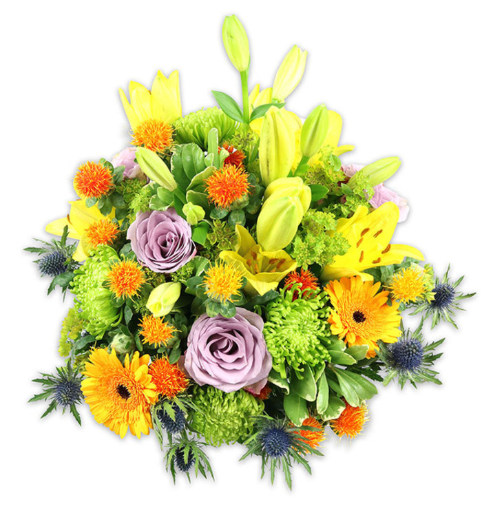 A richly textured, artfully balanced bouquet sits against a bright white field, each bloom chosen for colour, form and tactile contrast. Radiant yellow Asiatic lilies form vertical accents; a few burst fully open to show their freckled throats and pollen-dusted stamens, while others remain as elongated chartreuse buds that lend a graceful upward movement. Soft lavender roses are placed near the heart of the arrangement, their velveteen petals unfolding in layered spirals that calm the overall exuberance. Scattered among them, bold orange Gerbera daisies offer broad, flat petals and darker central discs that catch the eye, and clusters of lime-green button chrysanthemums supply dense, almost moss-like volume. Tiny round, spiky orange and golden accent flowers - reminiscent of Craspedia or small thistle-like blooms - dance through the composition, adding playful highlights. Distinctive blue-grey sea thistles (Eryngium) emerge at the edges and lower planes, their starry, spined heads introducing a crisp, architectural counterpoint to the softer blossoms. A tapestry of foliage - from wide, glossy leaves to slender, veined fillers - frames the bouquet and creates depth beneath soft, directional light. The arrangement carries the warm, optimistic tone of late spring: celebratory yet composed, fragrant with sweet lily and rose notes. Perfect as a generous gift or a statement centrepiece, it reflects the kind of seasonal, thoughtful design customers in Friern Barnet and neighbouring New Southgate ask for when seeking something both joyful and sophisticated for anniversaries, thank-yous, or heartfelt remembrance.